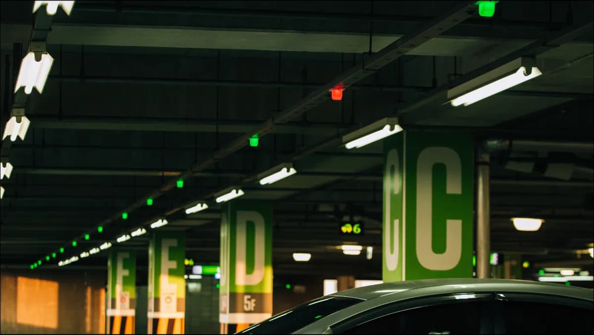 A modern multi-zone car park entrance at dusk with an RFID-equipped Android payment kiosk, a raised barrier showing 'Welcome' on a bilingual LED, and an ANPR camera mounted on the gantry above the lane.