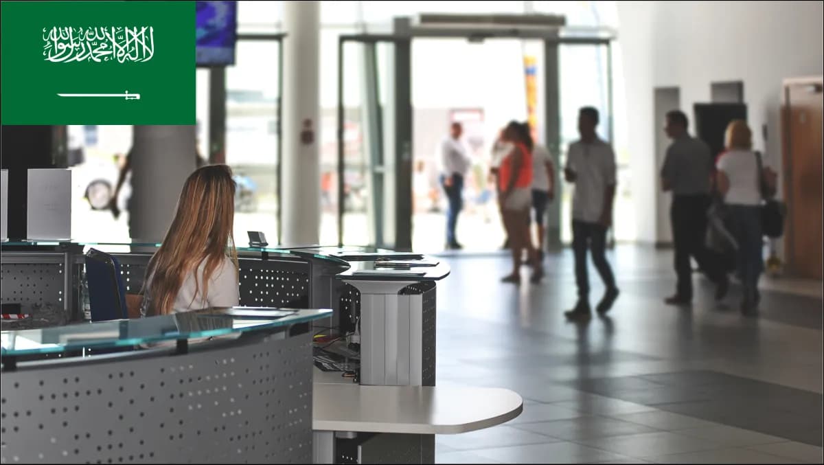 Citizen, contractor, and delegation visitors checking in at a Riyadh ministry lobby with bilingual Arabic-English kiosks and an accessible WCAG 2.2 AA host queue display.