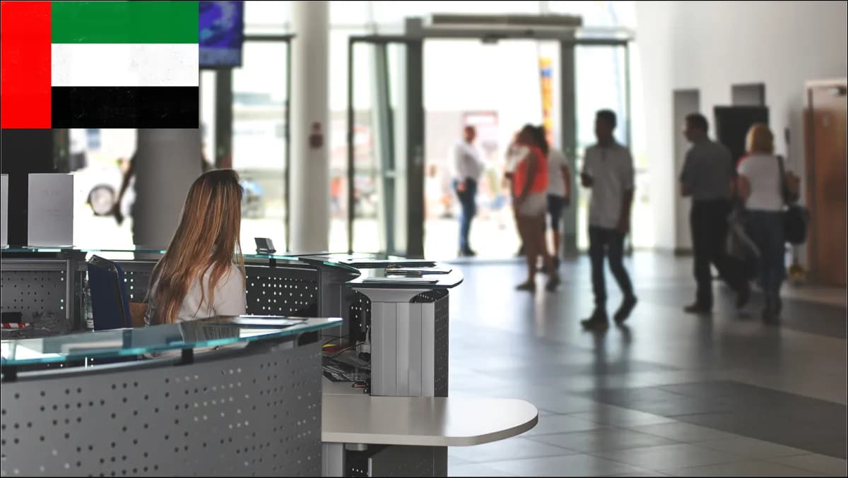 An Abu Dhabi federal ministry reception with bilingual Arabic and English signage, a self-service kiosk for citizens, a separate delegation channel, and a contractor check-in station with badge printing.